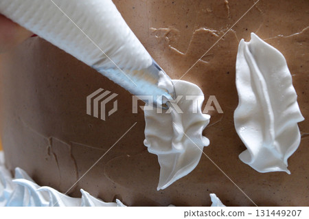 A woman pastry chef with a pastry bag in her hands squeezes cream on a cake in a home kitchen. Professional chef at work on bakery kitchen. culinary, baking and cooking food concept, home cooking A woman pastry chef with a pastry bag in her hands squeezes cream on a cake in a home kitchen. Professional chef at work on bakery kitchen. culinary, baking and cooking food concept, home cooking 131449207