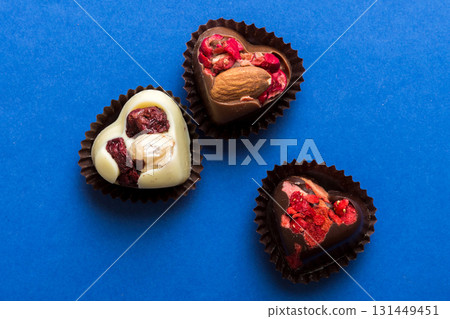 chocolate sweets in the form of a heart with fruits and nuts on a colored background. top view with space for text, holiday concept chocolate sweets in the form of a heart with fruits and nuts on a colored background. top view with space for text, holiday concept 131449451
