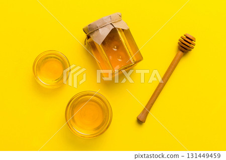 Glass jar of honey with wooden drizzler on colored background. Honey pot and dipper high above. Top view copy space Glass jar of honey with wooden drizzler on colored background. Honey pot and dipper high above. Top view copy space 131449459