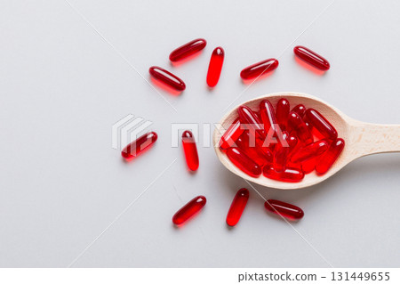 Vitamin capsules in a spoon on a colored background. Pills served as a healthy meal. Red soft gel vitamin supplement capsules on spoon 131449655