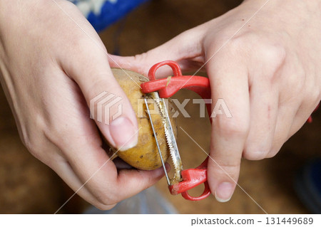 Woman peels potatoes while sitting on a chair in the kitchen 131449689