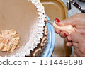 A woman pastry chef with a pastry bag in her hands squeezes cream on a cake in a home kitchen. Professional chef at work on bakery kitchen. culinary, baking and cooking food concept, home cooking 131449698