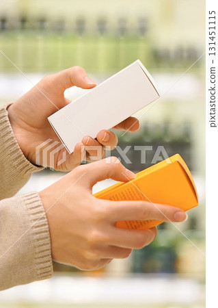 Close up of woman holding two cosmetic serums for face or hair in a beauty store, comparing products and reading labels. Female shopper choosing skincare or haircare item. Conscious choice. 131451115