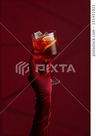 Stylish hand holding red cocktail against a rich red background, nightlife and party theme, premium drink concept  131451921