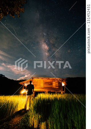 A hut in the middle of a rice field and the belly of a milky way, stars and a night sky with clouds 131452431