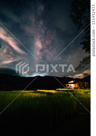 A hut in the middle of a rice field and the belly of a milky way, stars and a night sky with clouds 131452433