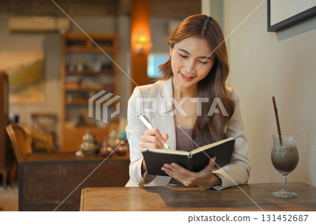 Businesswoman sitting in a cozy cafe while writing notes in a notebook 131452687