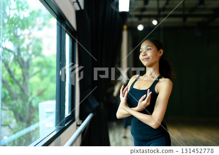 Graceful young ballerina practicing arm position near the barre in a dance studio Graceful young ballerina practicing arm position near the barre in a dance studio 131452778