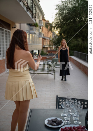 Woman taking photo of her friend on smartphone at outdoor terrace gathering Woman taking photo of her friend on smartphone at outdoor terrace gathering 131452922