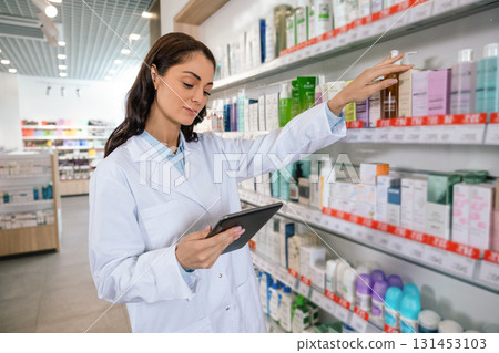Pharmacist woman conducting inventory with clipboard in drugstore 131453103