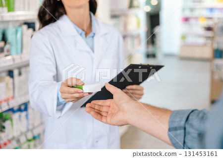 Unrecognizable woman pharmacist giving medicine to male client 131453161