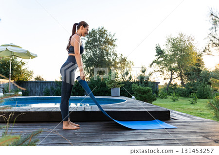 Slim woman in sportswear putting yoga mat on the ground 131453257