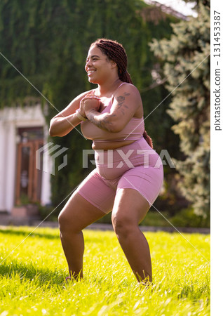 Plus size young woman doing squats on the lawn and looking determined 131453387