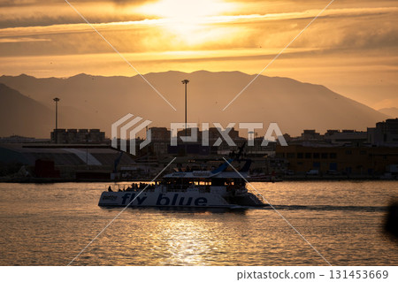 Spain Malaga 1 28 2024 Sunset maritime scene featuring 'Fly Blue' boat, silhouetted cityscape, warm tones and radiant sky Spain Malaga 1 28 2024 Sunset maritime scene featuring 'Fly Blue' boat, silhouetted cityscape, warm tones and radiant sky 131453669