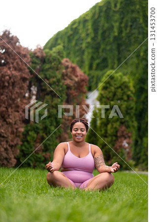 Woman in pink sportswear sitting on a grass on lotus pose and feeling good Woman in pink sportswear sitting on a grass on lotus pose and feeling good 131453700