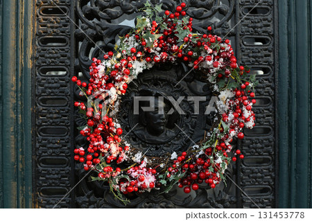 A Christmas wreath of red berries on a metal door with a bas-relief portrait of a man A Christmas wreath of red berries on a metal door with a bas-relief portrait of a man 131453778