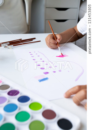 Child painting with watercolors on white paper in art studio setting 131453805