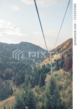 A scenic view from a cable car traveling over mountains. Lush green trees and rocky hills are visible under a clear sky. Ideal for vacation imagery. A scenic view from a cable car traveling over mountains. Lush green trees and rocky hills are visible under a clear sky. Ideal for vacation imagery. 131454360