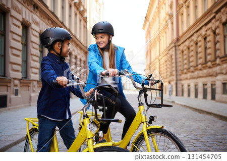 Two young cyclists wearing helmets are chatting on yellow rental bikes in a European city 131454705