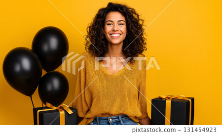 Happy satisfied smiling girl in 90s retro style on a yellow background with black balloons and black packages. Consumerism, sales, black friday. Online shopping. 131454923
