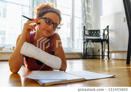 Teenage girl with broken arm in cast, wearing glasses, doing homework, at home Teenage girl with broken arm in cast, wearing glasses, doing homework, at home 131455605