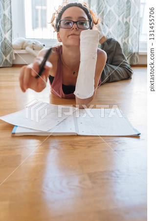 Teenage girl with broken arm in cast, wearing glasses, doing homework, at home Teenage girl with broken arm in cast, wearing glasses, doing homework, at home 131455706