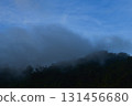 Fog covering dark forest mountains with blue sky above 131456680