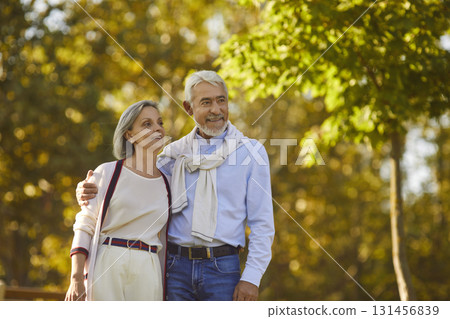 Happy married elderly man and woman are walking together in green park in summer Happy married elderly man and woman are walking together in green park in summer 131456839