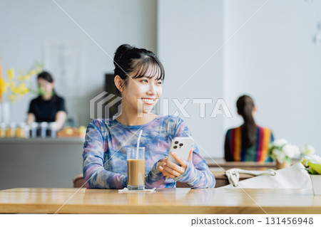 一個年輕的女人,看著一家咖啡館的智能手機 一個年輕的女人,看著一家咖啡館的智能手機 131456948