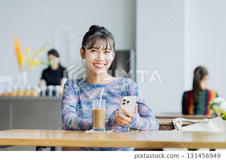 一個年輕的女人,看著一家咖啡館的智能手機 一個年輕的女人,看著一家咖啡館的智能手機 131456949