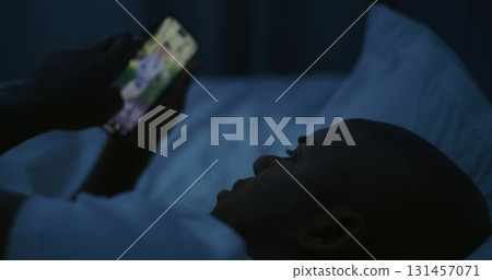 Night, Man Lies in Bed Under Dim Light and Scrolls Endlessly Through Social Media on Smartphone Night, Man Lies in Bed Under Dim Light and Scrolls Endlessly Through Social Media on Smartphone 131457071
