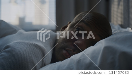 Man Slowly Waking Up in Bed, Resting Head on White Pillow, in Soft Morning Light Man Slowly Waking Up in Bed, Resting Head on White Pillow, in Soft Morning Light 131457083