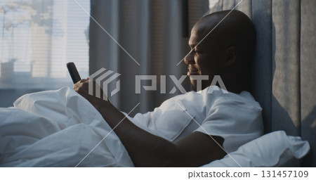 Peaceful Morning Moment Focused Man in Bed With Smartphone, Smiling Screen 131457109