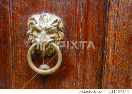 Brass door knocker in the shape of a lion holding a ring in its teeth. Wooden copy space background 131457344