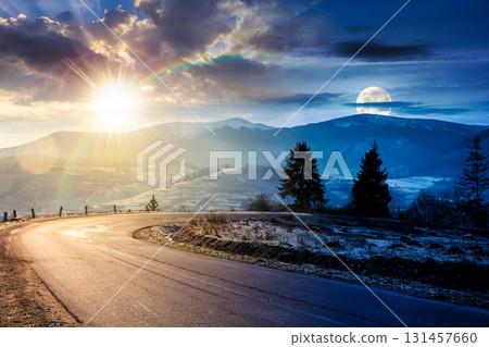 country road in mountains. day and night time change concept. beautiful countryside landscape in late autumn. fir trees on the roadside with sun and moon. scenic view of distant ridge in snow 131457660