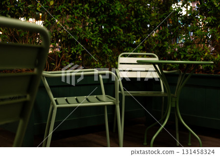 Inviting cafe terrace at night, featuring minimalistic green chairs and plants under soft lights, offering quiet escape for those seeking solitude in urban setting with intimate vibe Inviting cafe terrace at night, featuring minimalistic green chairs and plants under soft lights, offering quiet escape for those seeking solitude in urban setting with intimate vibe 131458324