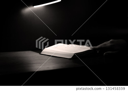 Hand gently turning pages of open book, bathed in soft. Quiet, intimate atmosphere evokes sense of reflection, deep thought, and emotional connection with content, perfect for personal discovery 131458339