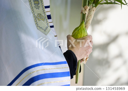 Succot. Jewish man in a Tallit praying while waving the Four Species, Lulav and Etrog 131458969