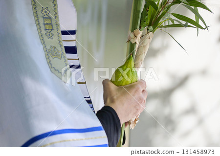 Succot. Jewish man in a Tallit praying while waving the Four Species, Lulav and Etrog 131458973