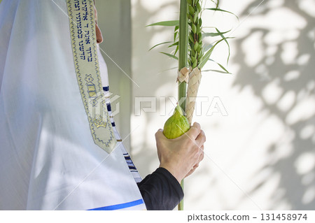 Succot. Jewish man in a Tallit praying while waving the Four Species, Lulav and Etrog 131458974