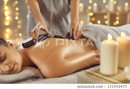 Beautiful young woman getting back massage at a spa salon with hot stones. 131459473