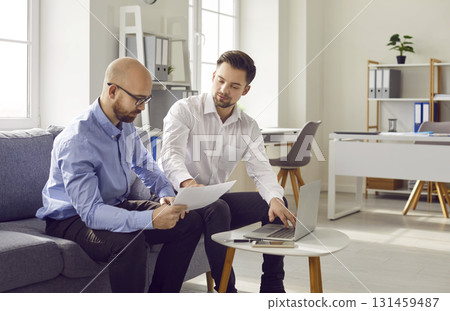 Two young business men sitting on sofa work in office talking and having discussion. 131459487
