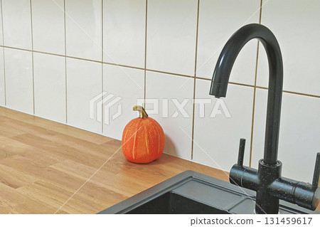 Minimalist kitchen with black faucet and small pumpkin on wooden counter against white tiles Minimalist kitchen with black faucet and small pumpkin on wooden counter against white tiles 131459617