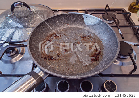 Greasy non stick pan on gas stove after cooking, brown residue in center, cleanup pending Greasy non stick pan on gas stove after cooking, brown residue in center, cleanup pending 131459625