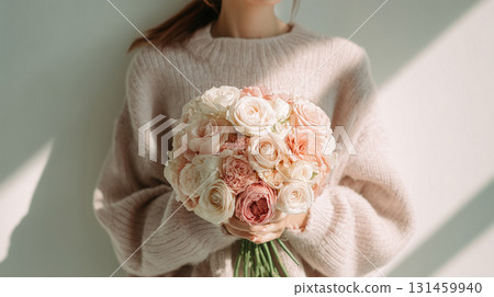 A woman in a light sweater gently holds a bouquet of roses 131459940