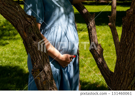 Pregnant woman standing among trees holding her belly Pregnant woman standing among trees holding her belly 131460061
