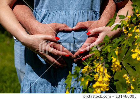 Pregnant couple forming heart with hands on baby bump in spring 131460095