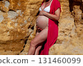 Pregnant woman in bikini leaning on rocky cliff in sunlight 131460099