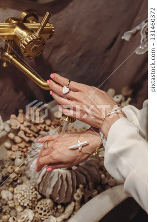 Young woman washing hands at seashell-decorated washbasin with fashionable pearl beads Young woman washing hands at seashell-decorated washbasin with fashionable pearl beads 131460372