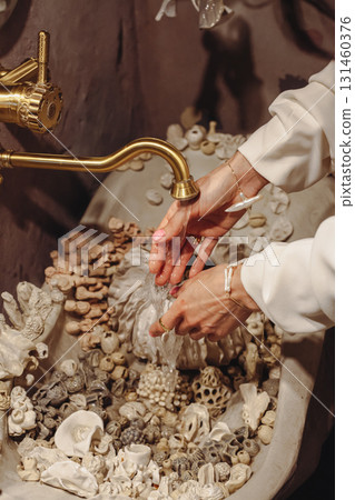 Young woman washes her hands in a seashell decorated washbasin with unique pearl beads Young woman washes her hands in a seashell decorated washbasin with unique pearl beads 131460376